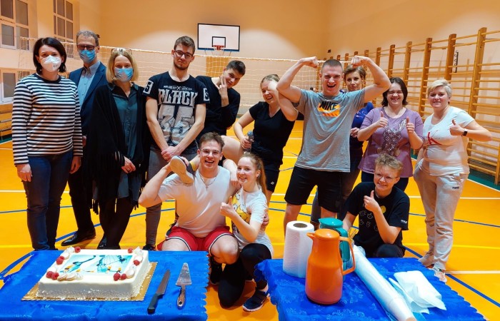 Grupowe zdjęcie uczniów na hali sportowej z tortem.