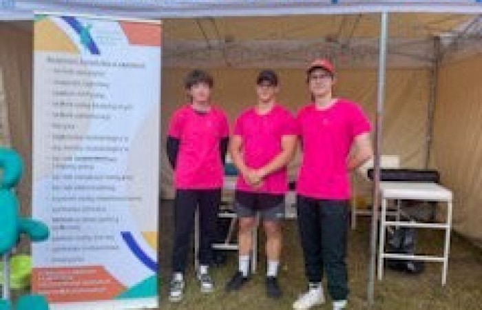 Trzech uczniów przy banerze szkoły w różowych koszulach.