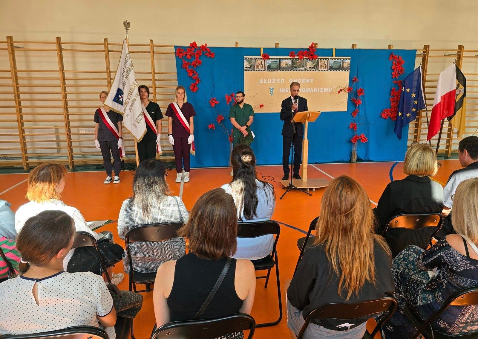 Widok na sztandar szkoły wraz z przemawiającym Dyrektorem.