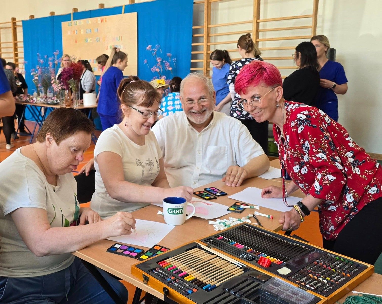 Nauczyciel prowadzi z seniorami race plastyczne przy stole.