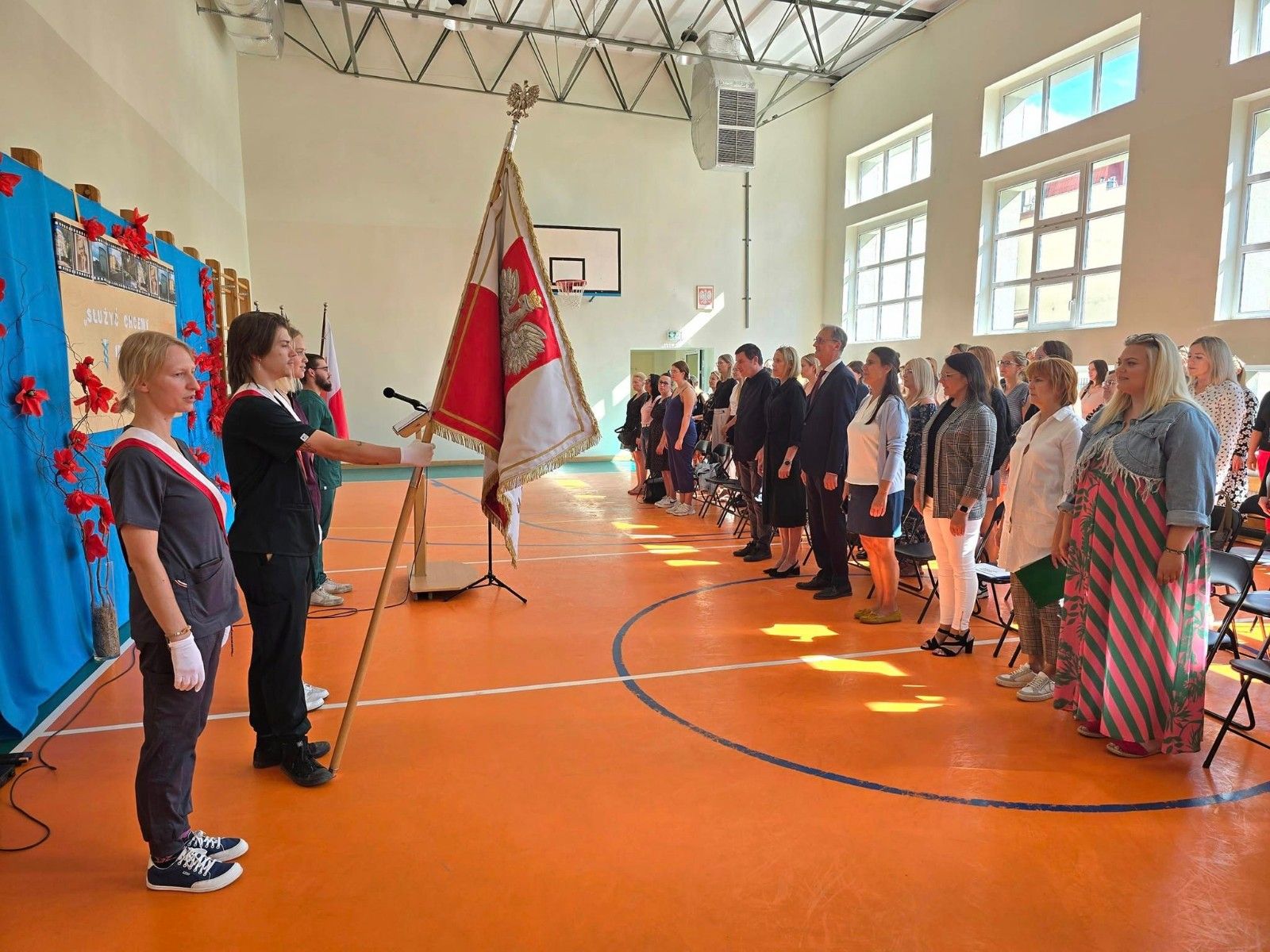 Widok na sztandar szkoły wraz z przybyłymi gości, uczniami i kadrą pedagogiczną.