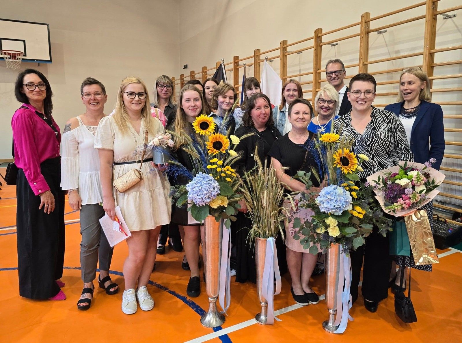 Wspólne zdjęcie uczniów i nauczycieli z kwiatami.