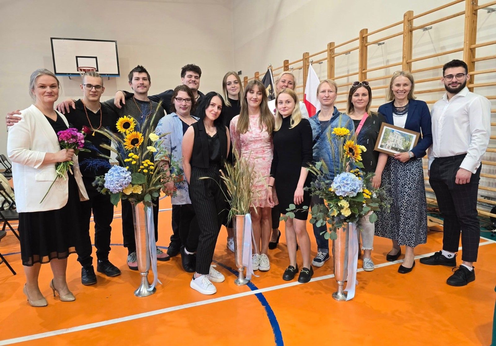 Wspólne zdjęcie uczniów i nauczycieli z kwiatami.