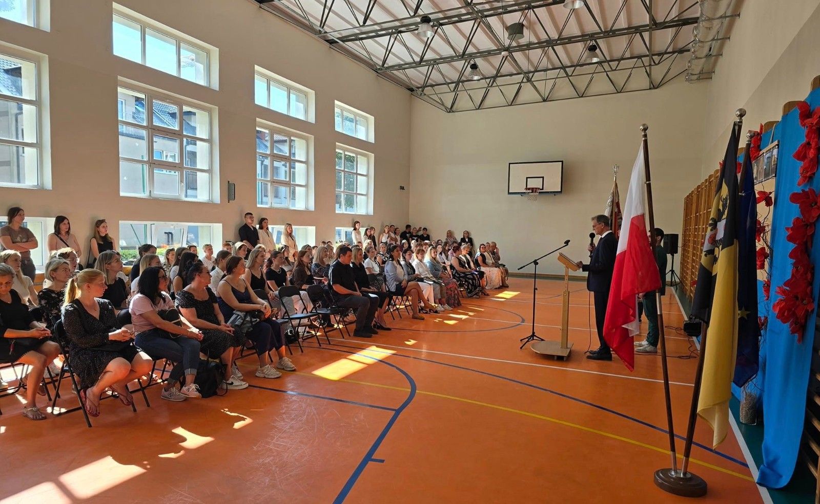 Widok na uczniów oraz nauczycieli na hali sportowej podczas rozpoczęcia roku.