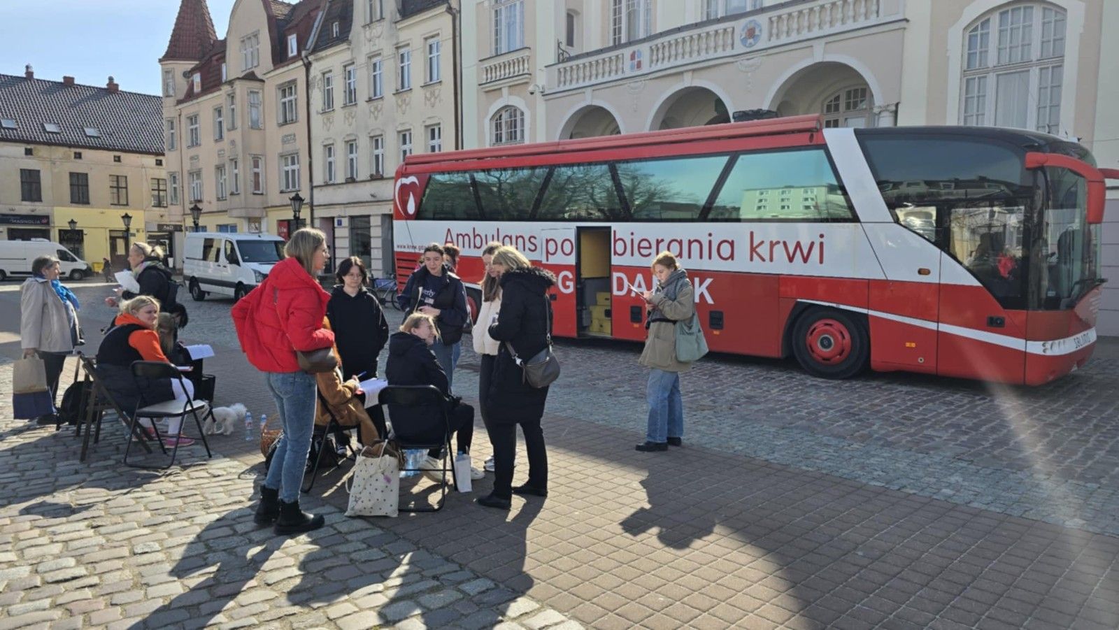 Widok z dalszej perspektywy na autobus i uczestników zbiórki krwi.