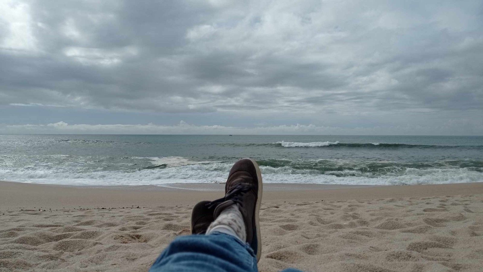 Widok na pochmurną plażę wraz z wzburzonym morzem.