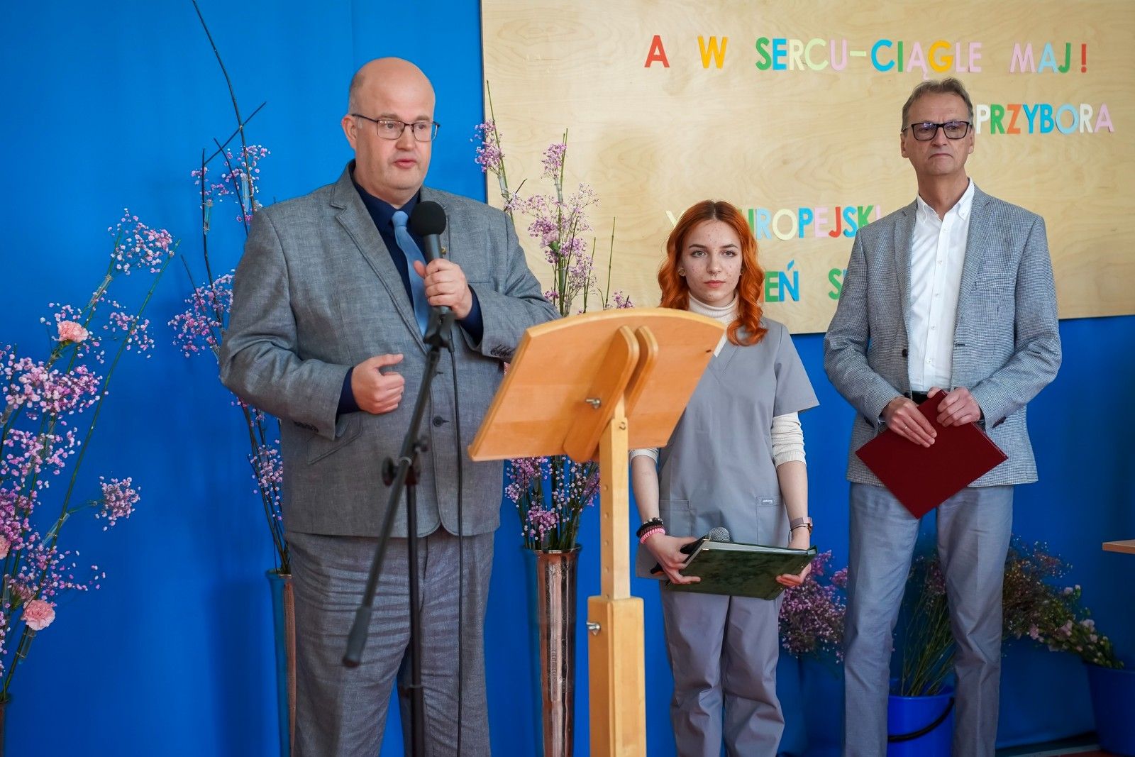 Przemawiający starosta w tle Dyrektor szkoły wraz zuczennicą.