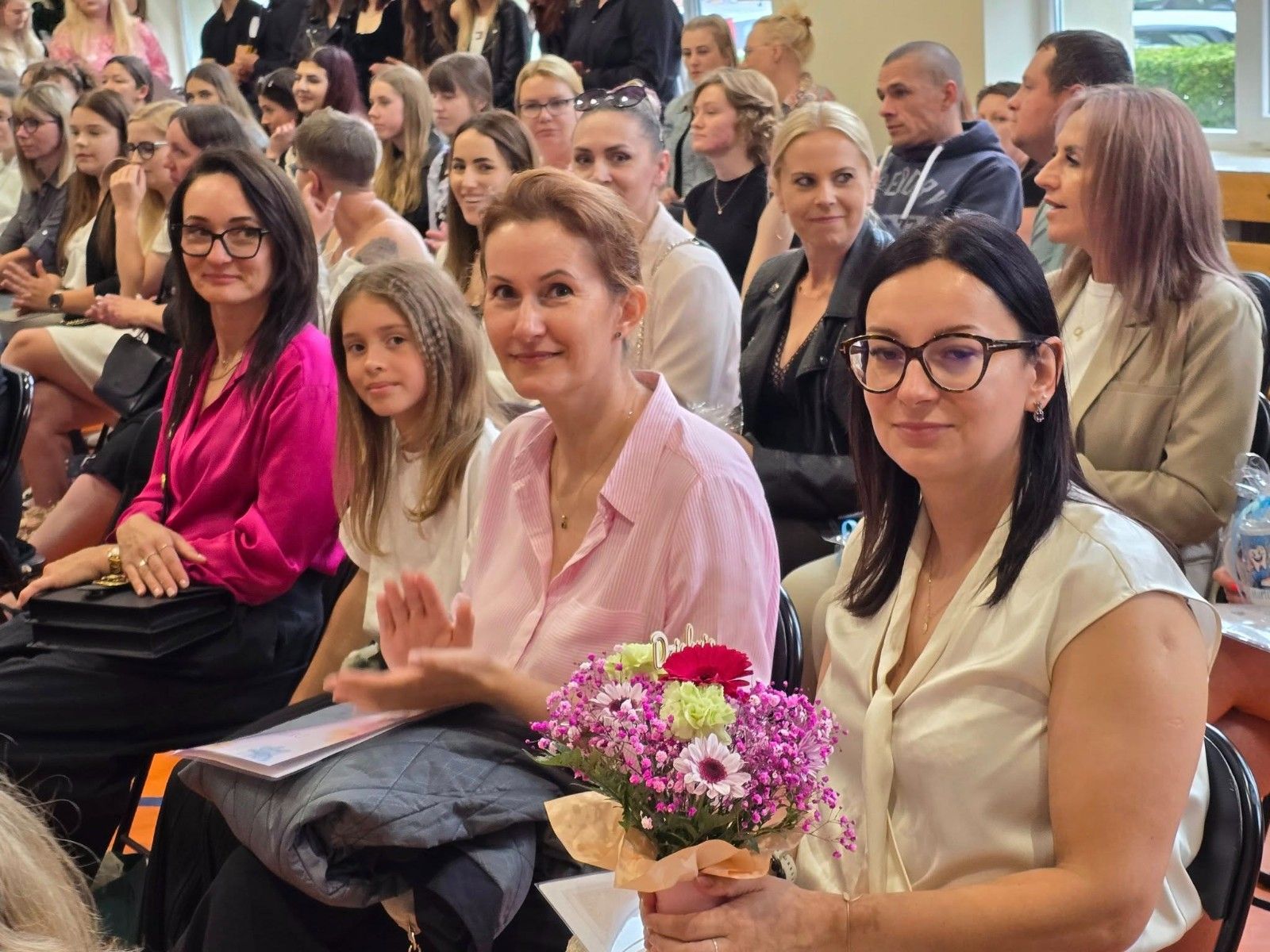 Wspólne zdjęcie uczniów i nauczycieli z kwiatami.