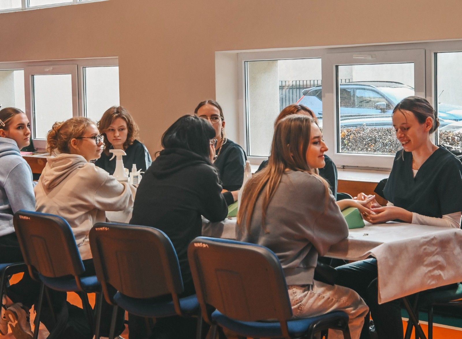 Widok na stół z uczniami wykonującymi zabiegi estetyczne rąk.