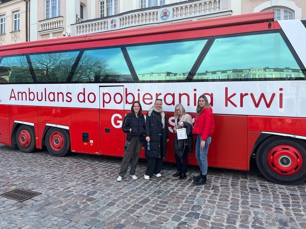 Grupowe zdjęcie na tle z autobusem do oddawania krwi.