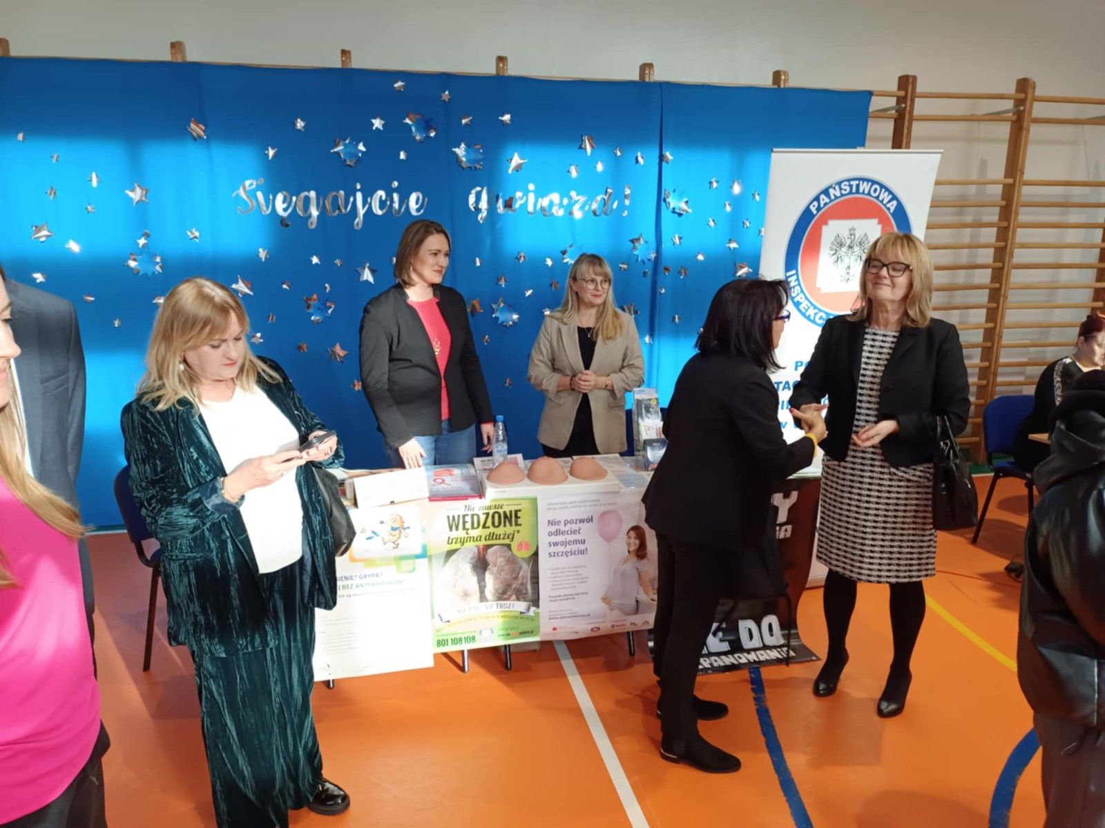 Widok na stoisko Państwowej Inspekcji Pracy na hali sportowej.