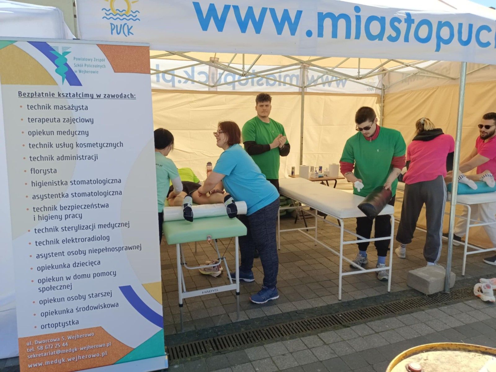 Uczniowie wykonujący w namiocie masarz nóg uczestnikom biegu. Plakat szkoły.