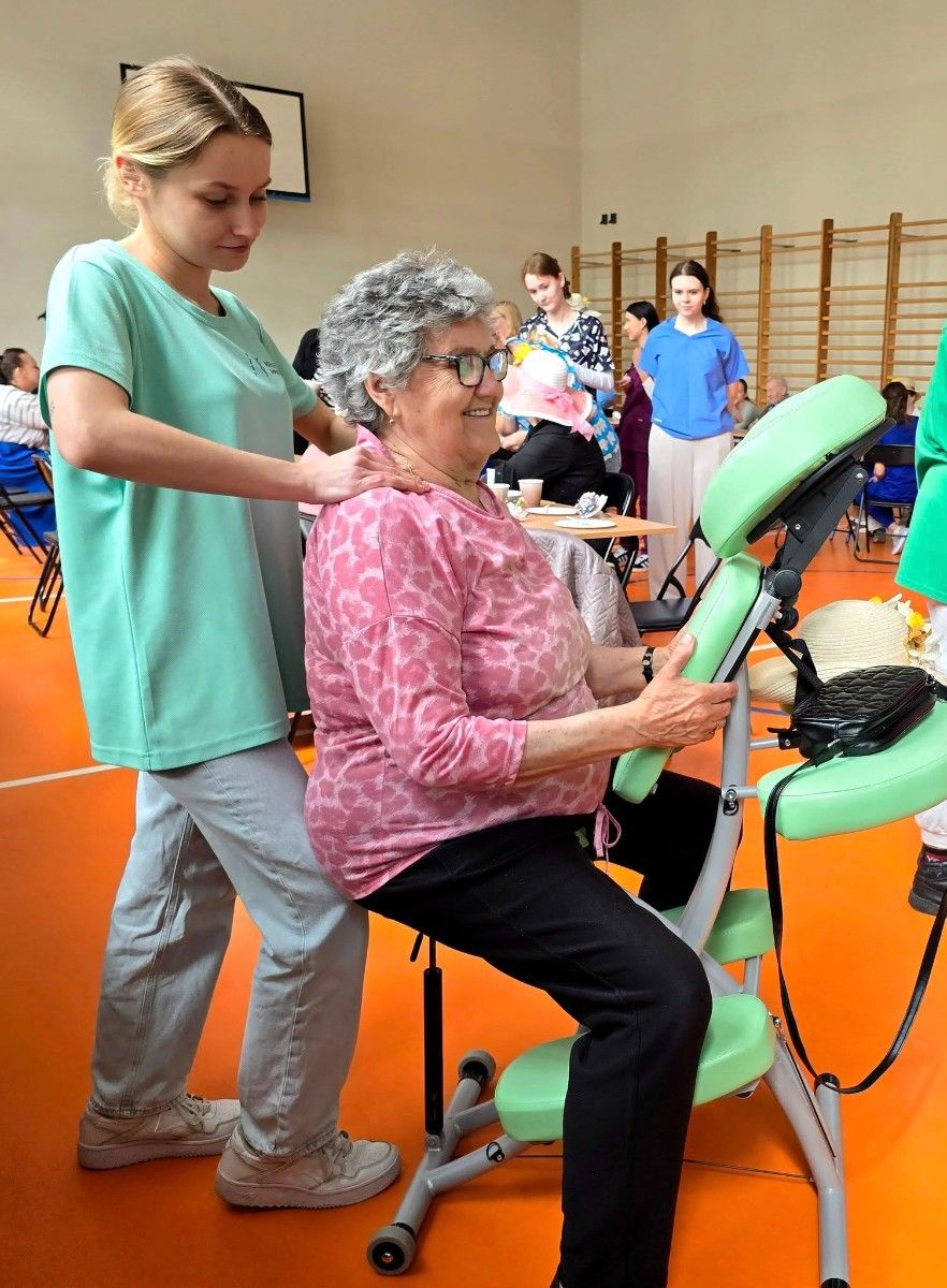 Uczennica wykonująca masarz barków seniorce na krześle do masażu.