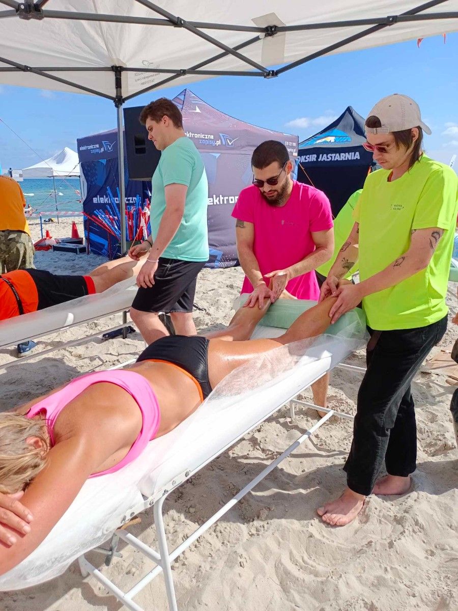 Uczennice masujące sportowca na plaży na stole do masażu. 