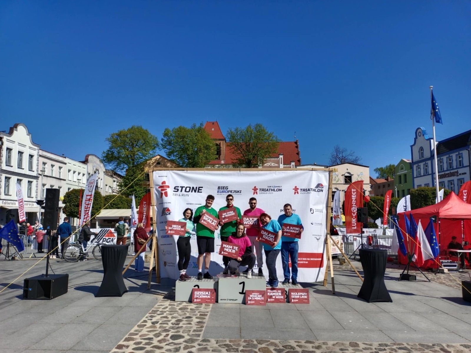 Uczniowie stojący na podium na rynku z tabliczkami.