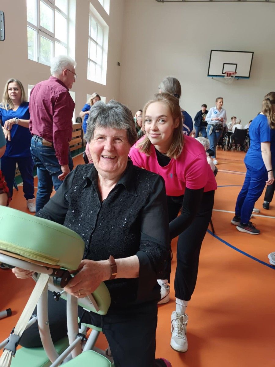 Uczennica wykonująca masarz pleców uśmiechniętej seniorce.