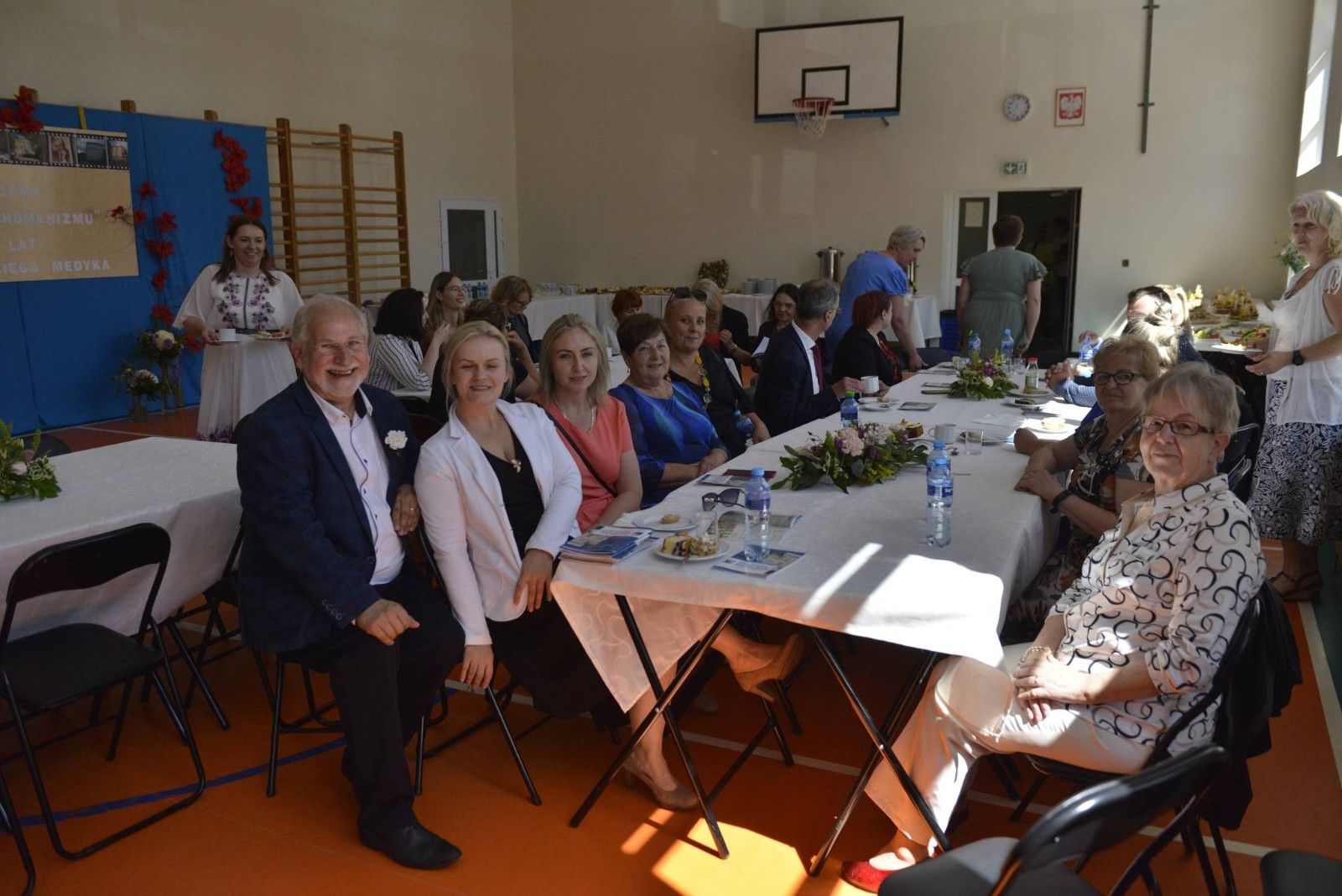 Zdjęcie gości przy stołach na hali sportowej.