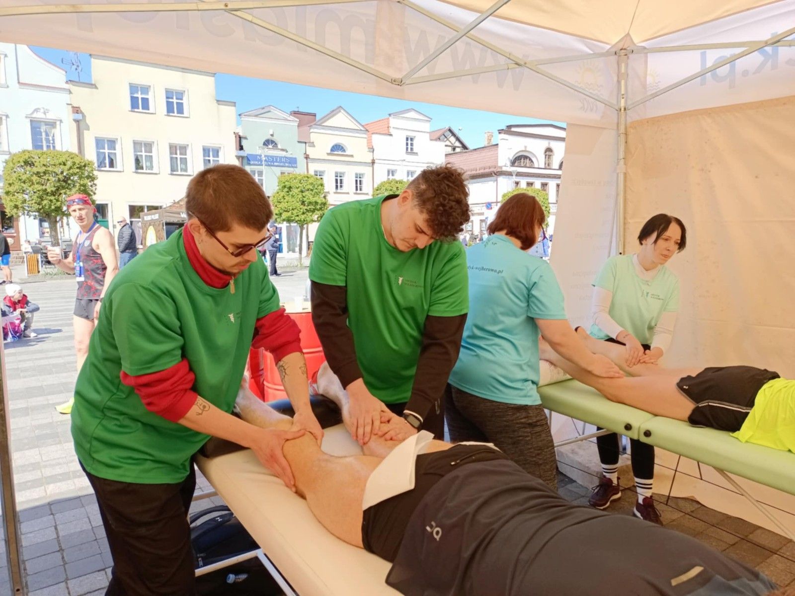 Uczniowie wykonujący w namiocie masarz nóg uczestnikom biegu.