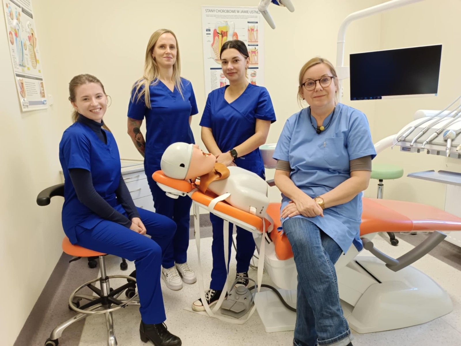 Wspólne zdjęcie uczniów wraz z nauczycielem przy fotelu dentystycznym z manekinem.