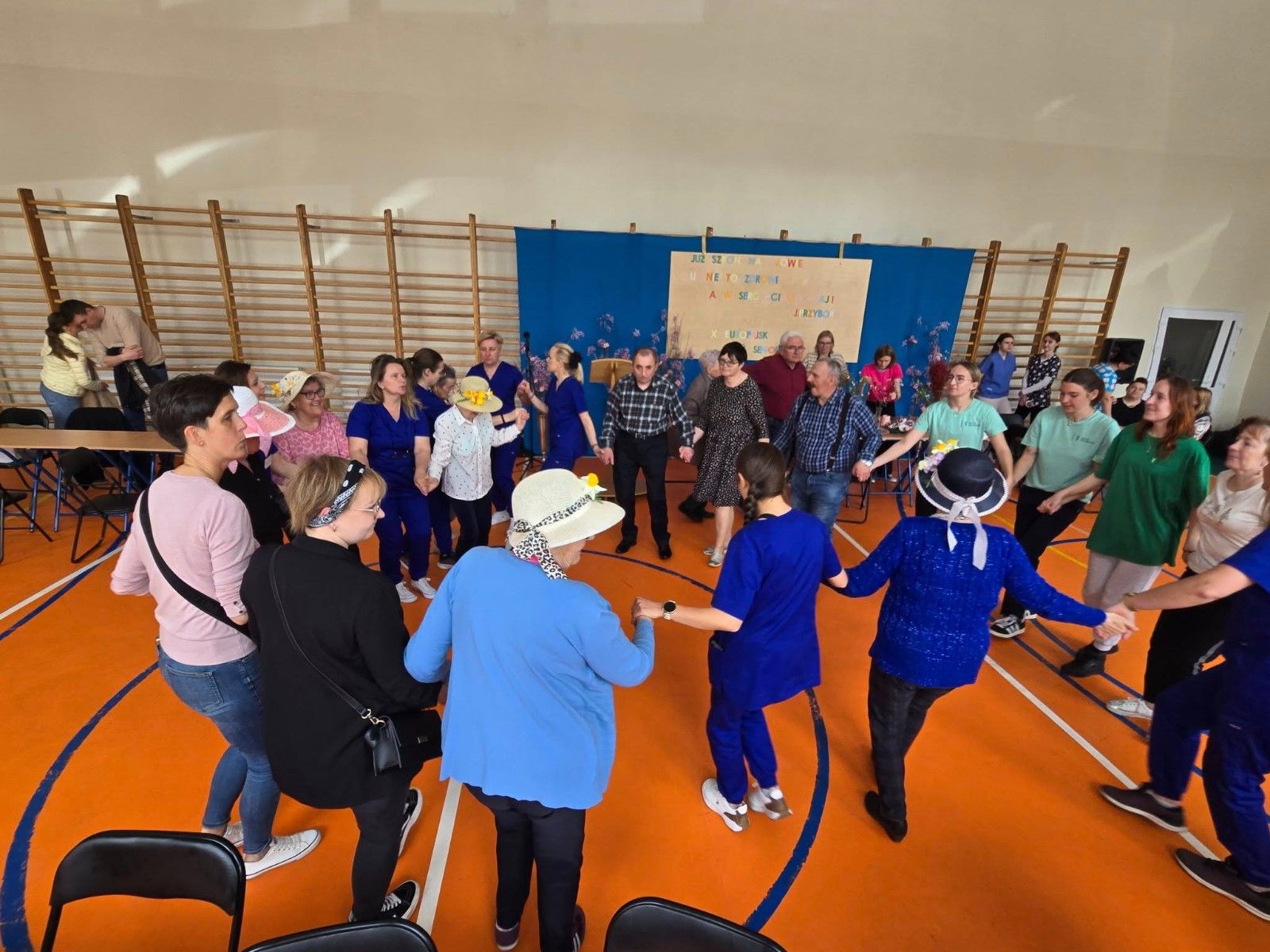 Seniorzy tańczący w kole - wspólna zabawa z uczniami.