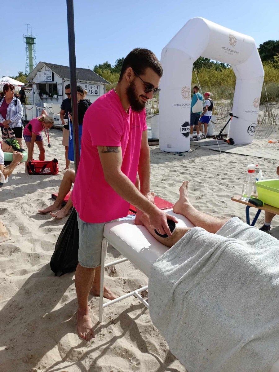 Uczennice masujące sportowców na plaży na stole do masażu. 
