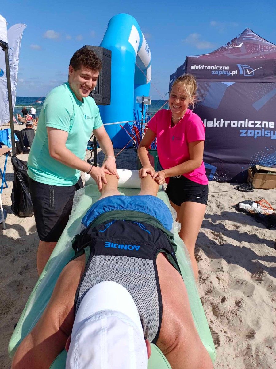 Uczennice masujące sportowców na plaży na stole do masażu. 