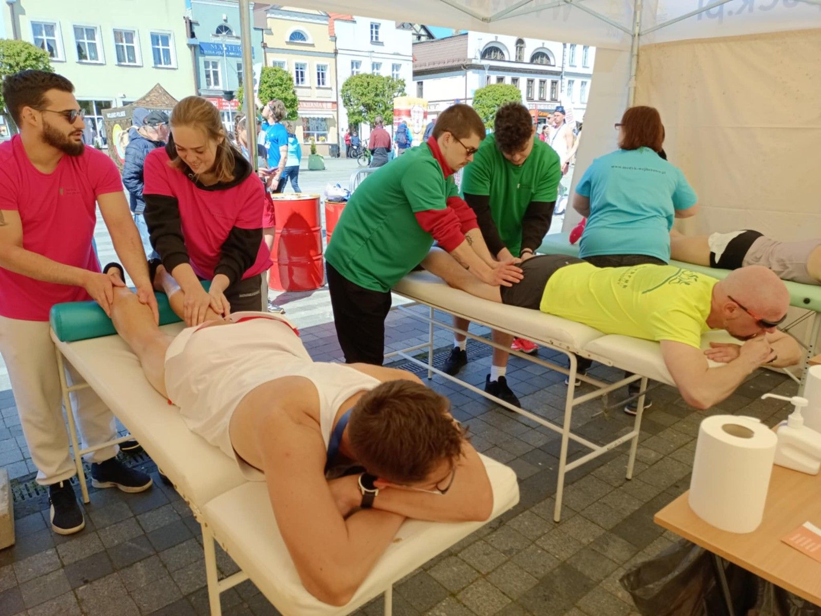 Uczniowie wykonujący w namiocie masarz nóg uczestnikom biegu.