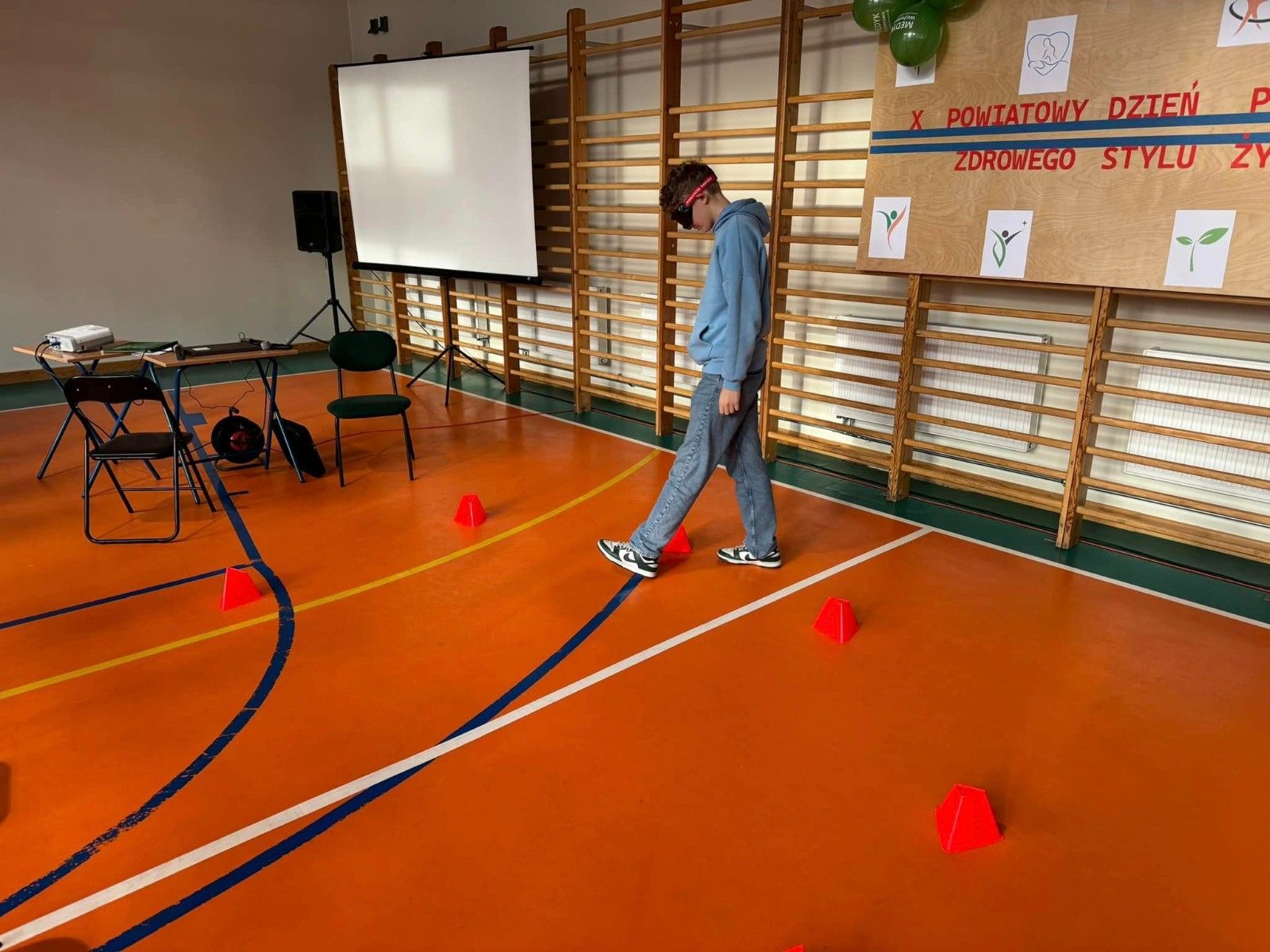 Widok na ucznia na hali sportowej wykonujący ćwiczenie z pachołkami w okularach sportowych..