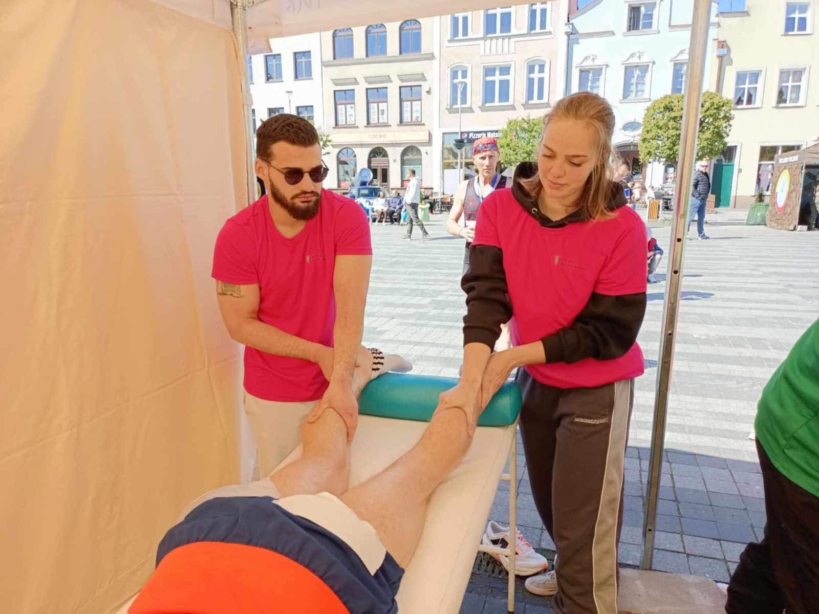 Uczniowie wykonujący w namiocie masarz nóg uczestnikom biegu.