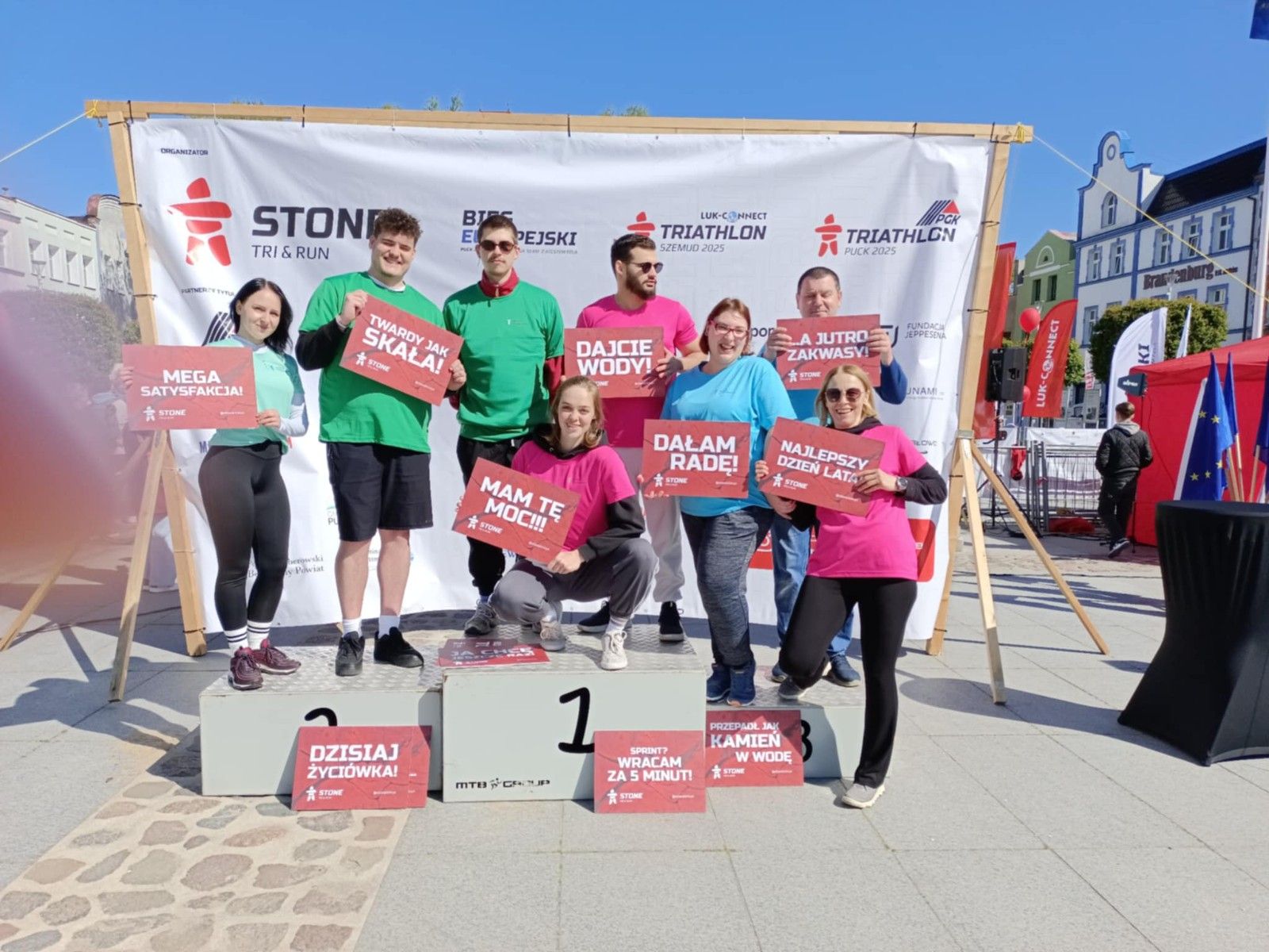 Uczniowie stojący na podium na rynku z tabliczkami.