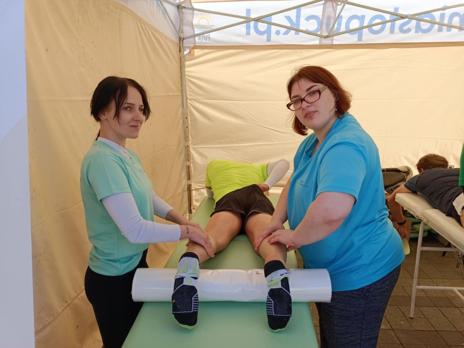 Uczniowie wykonujący w namiocie masarz nóg uczestnikom biegu.