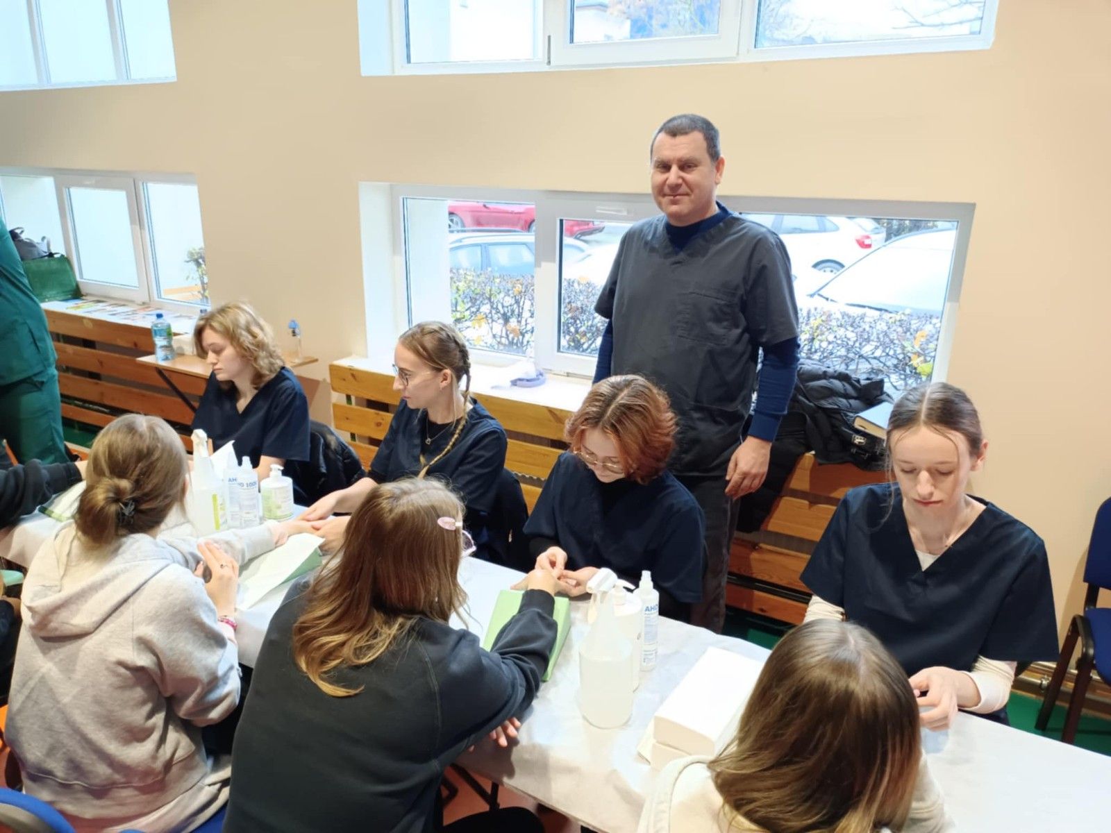 Widok na stół z uczniami wykonującymi zabiegi kosmetyczne rąk.