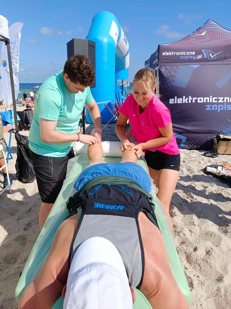 Uczennice masujące sportowców na plaży na stole do masażu. 