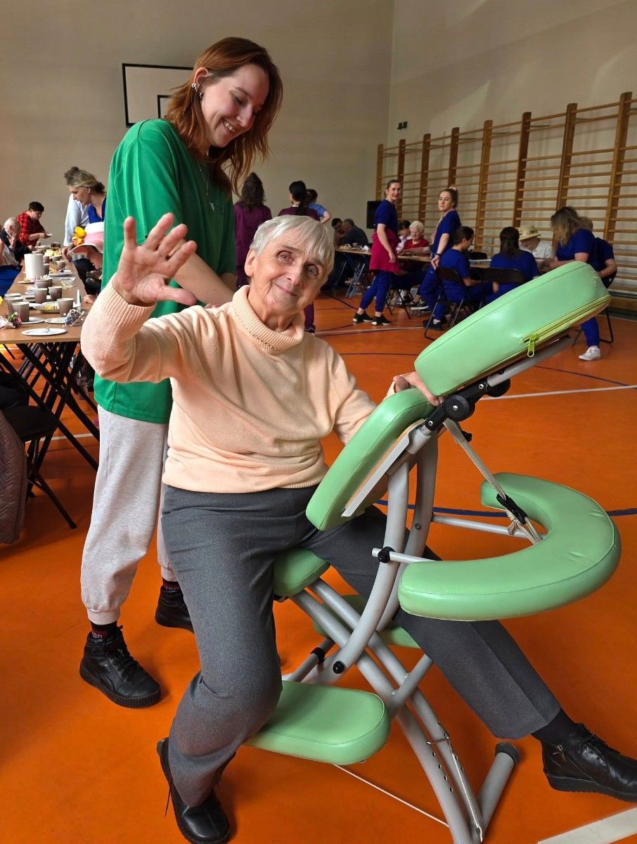 Uczennica wykonująca masarz pleców uśmiechniętej seniorce.