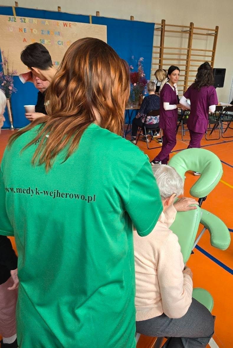 Widok na uczennicę wykonująca masarz seniorce.